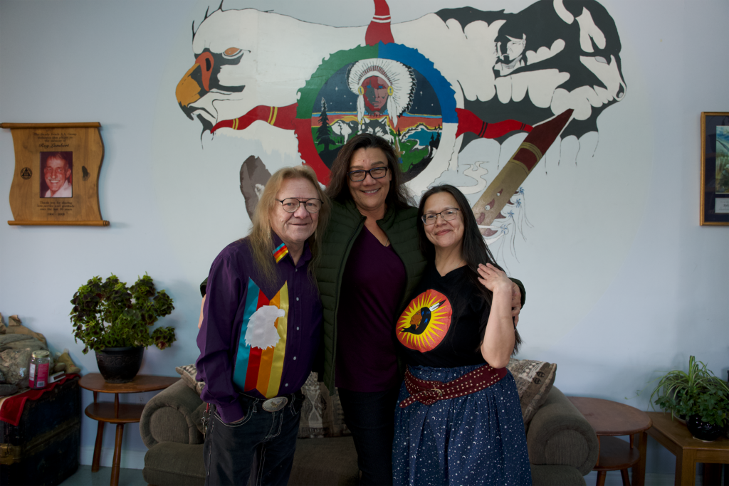 Pictured from left to right: Ken, Denise, and Kecia, standing together in front of a mural.