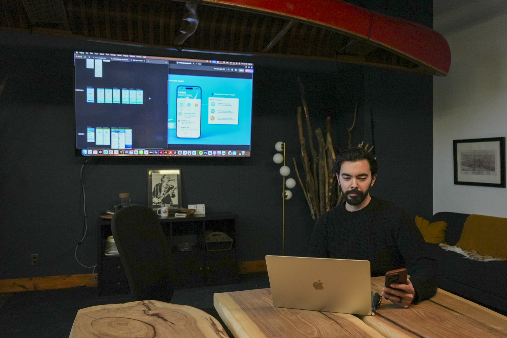 bearded man looking at laptop with tv in the background